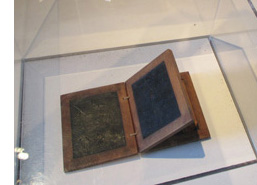 Photo shows three small boards hinged together.  Each board has a thin wooden frame surrounding a flat layer of black wax.